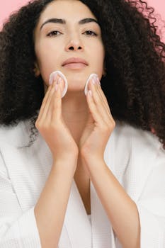Portrait of a woman in a white bathrobe gently cleansing her face with cotton pads.