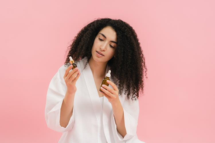 A Woman In White Robe Holding A Glass Bottles