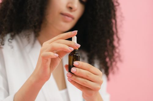 Free Close-up of woman holding a glass dropper bottle for skincare against a pink background. Stock Photo