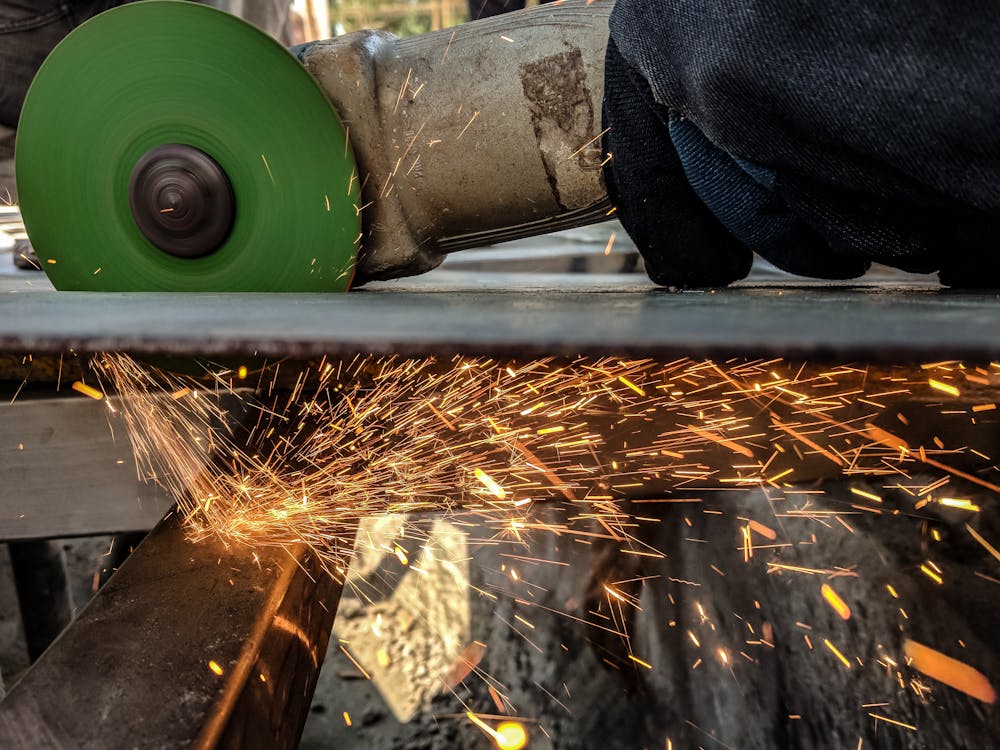 Person Using Green And Grey Angle Grinder On Sheet Of Metal