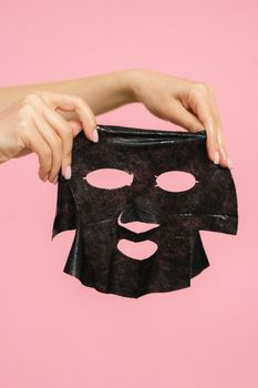 Close-up of hands holding a black sheet face mask, perfect for skincare and beauty routines.