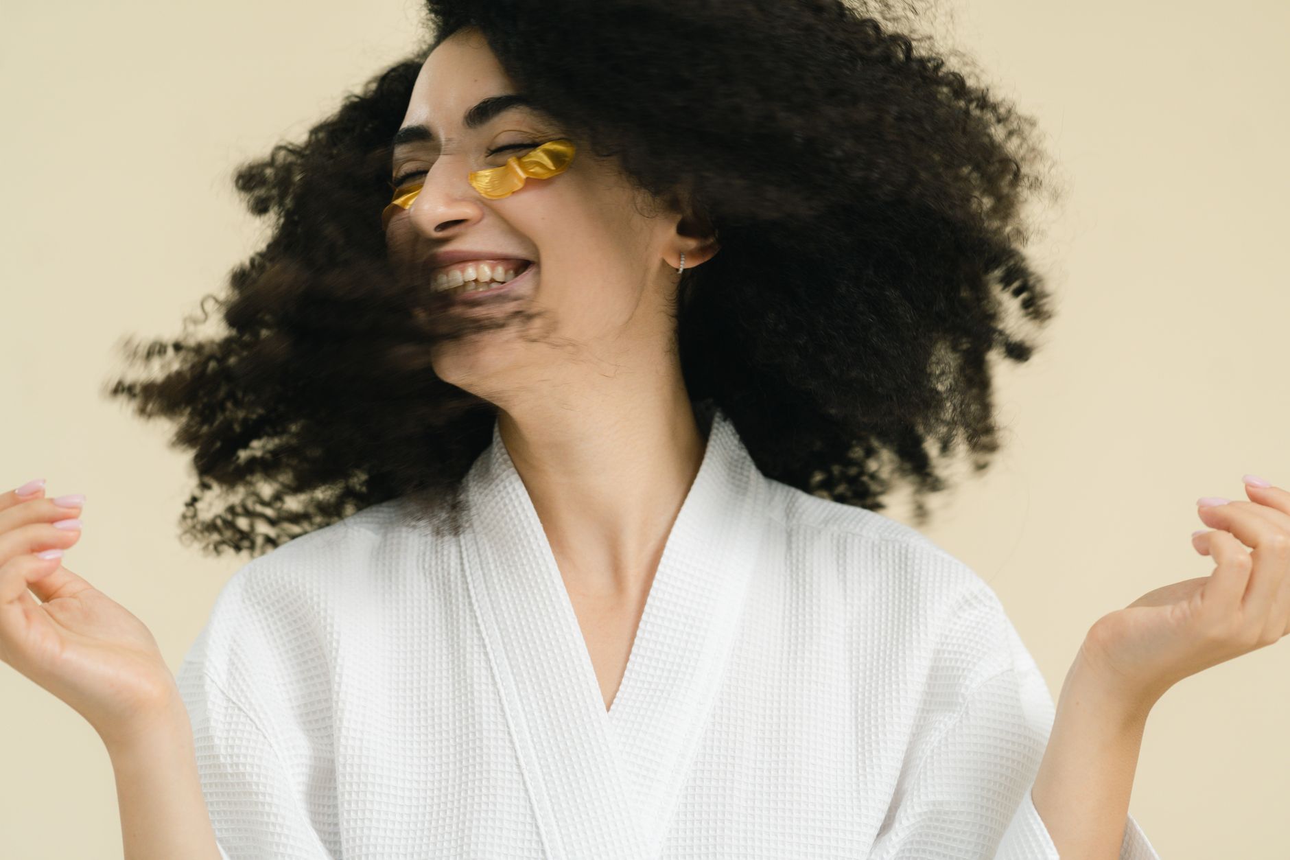 A young woman enjoys self-care with under-eye patches and a joyful smile.