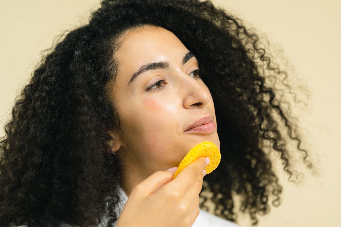 Free Woman Wiping a Yellow Sponge on Her Chin Stock Photo