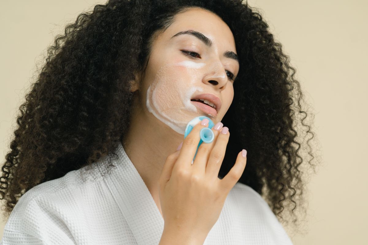 A woman massaging facial cleanser onto her cheek with a cleansing brush