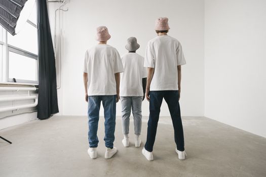 Three men in bucket hats and white shirts standing in a minimalist studio.