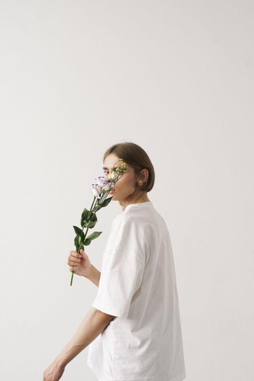 Free A serene portrait of a woman in a white shirt holding flowers on a white background. Stock Photo