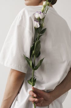 A minimalist portrait featuring a person in a white shirt holding delicate white flowers against a white backdrop.