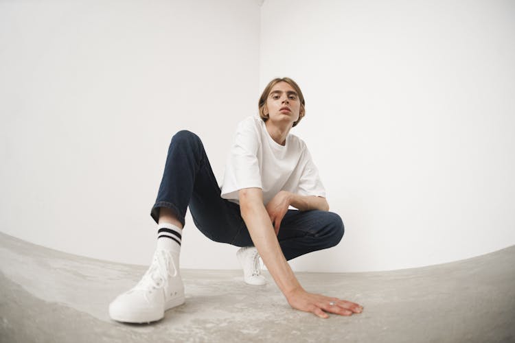 A Man Wearing A White Shirt And Denim Pants Crouching