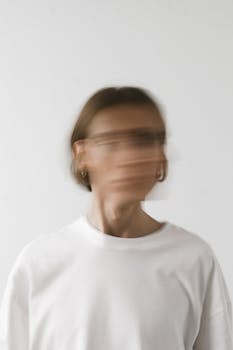 Artistic blurred portrait of an unrecognizable person wearing a white shirt on a white background.