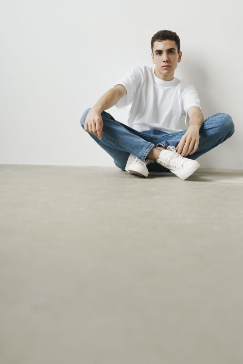 Free A young man in casual jeans and white sneakers poses in a minimalist indoor space. Stock Photo