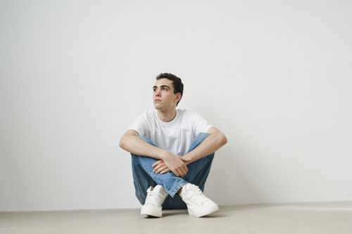 Free Young man posing casually in a white shirt and jeans against a minimalist white background. Stock Photo