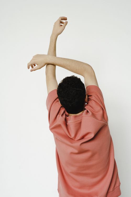 Free An adult man wearing a pink shirt stretches arms overhead against a white backdrop. Stock Photo