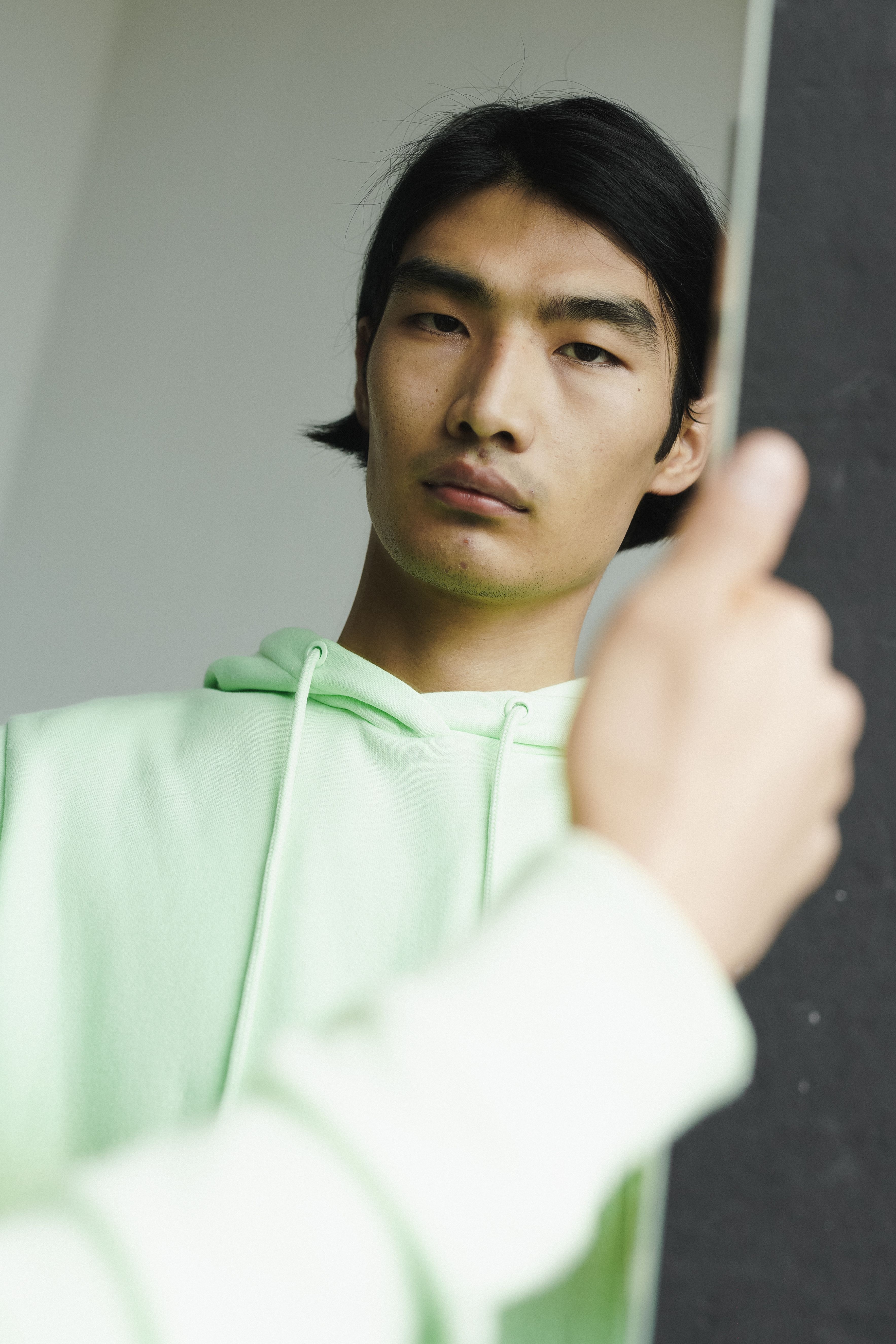 Close-up of a man in a green hoodie looking into a mirror with a serious expression.