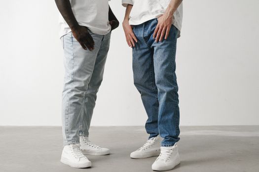 Close-up of two individuals wearing jeans and white sneakers in a minimalist setting.