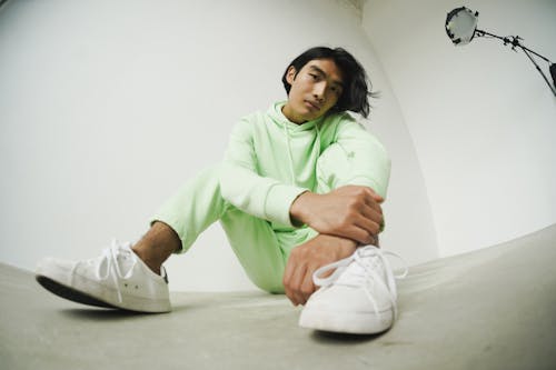 Low-Angle Shot of a Man in Green Hoodie Sitting on the Floor