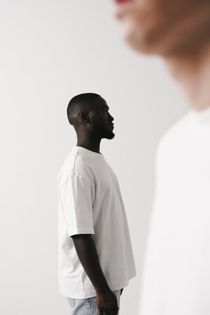 Minimalist side profile portrait of a stylish man in white shirt and denim, with a blurred foreground figure.