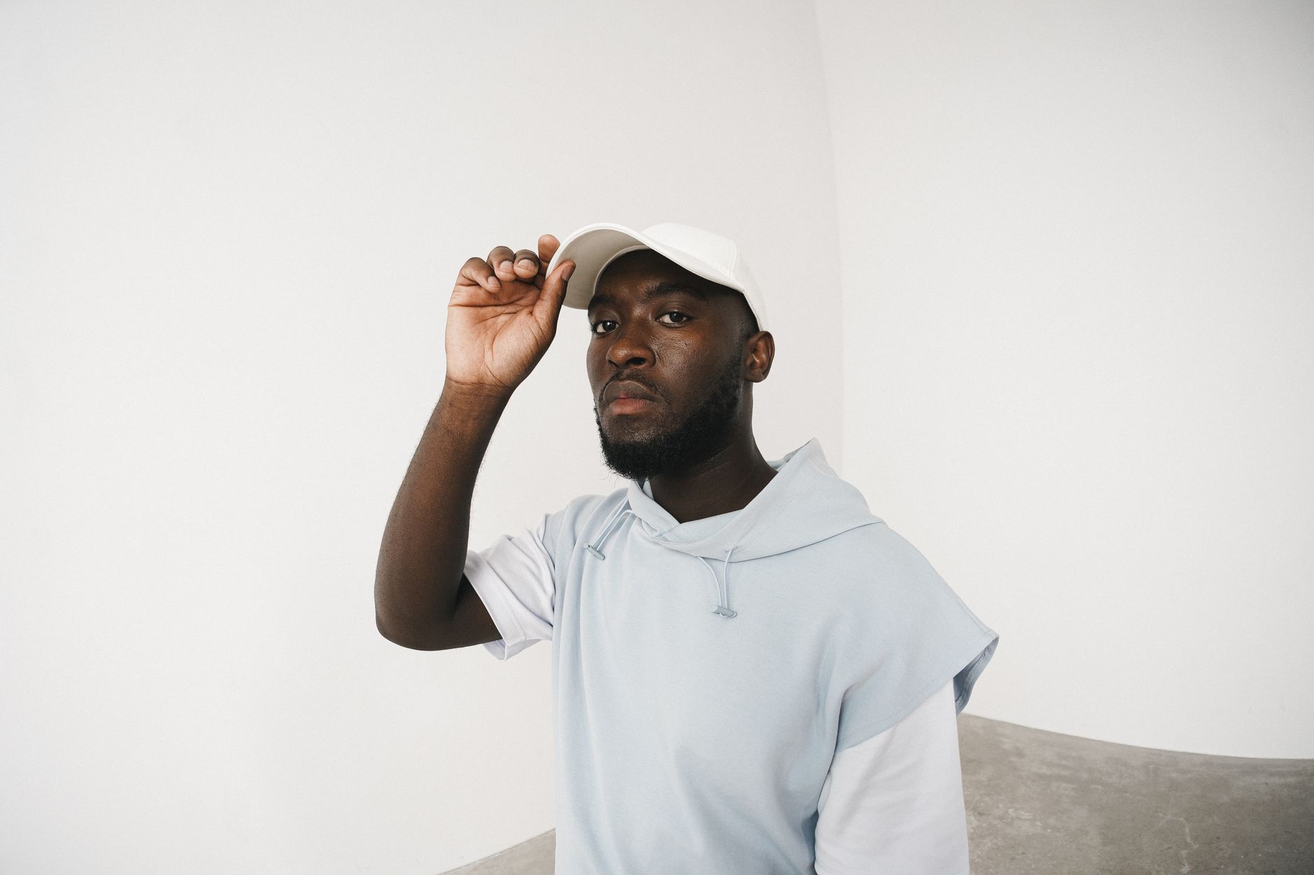 Homme en hoodie streetwear ajustant sa casquette blanche, look festival urbain épuré