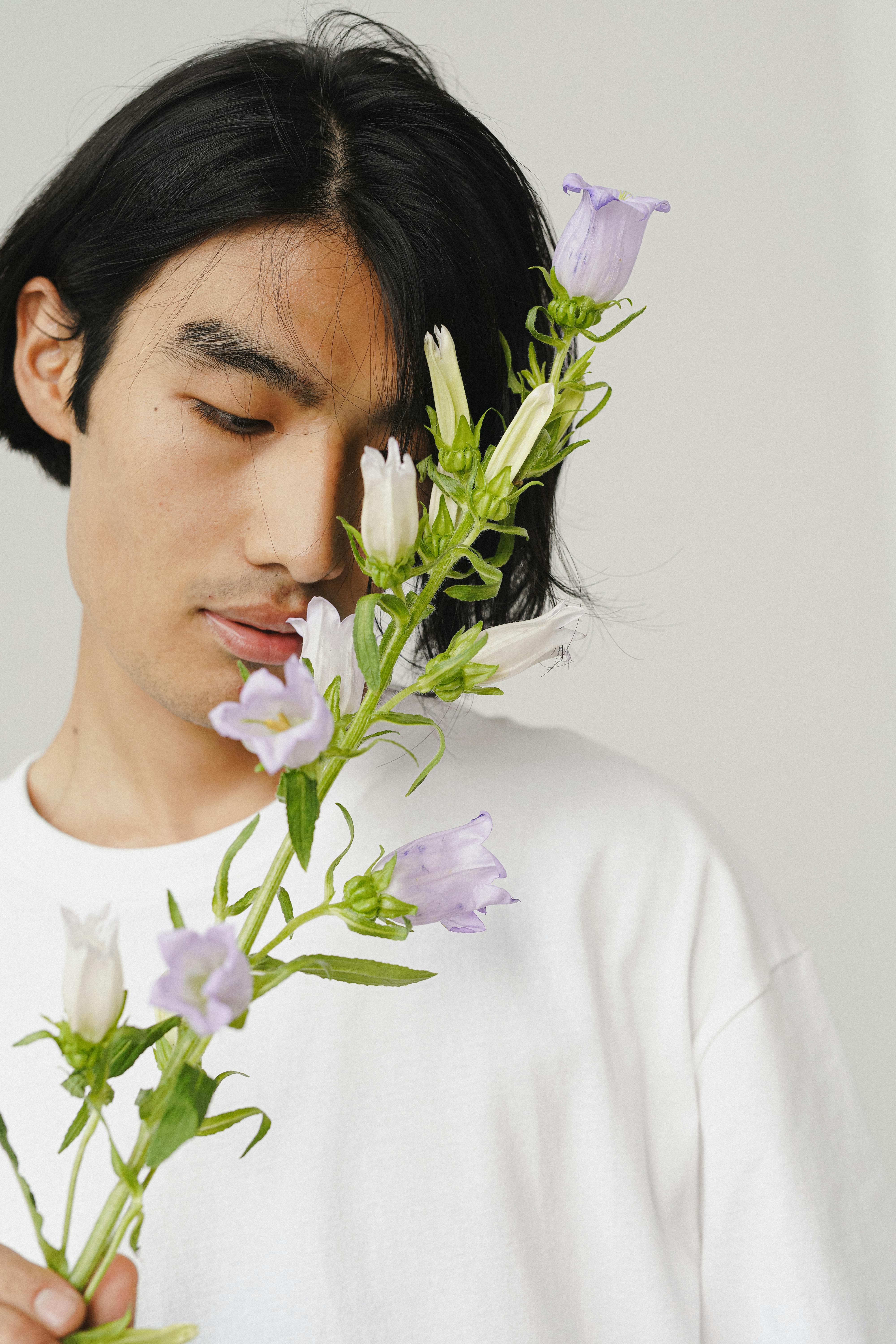 Portrait of an Asian man in a white shirt holding delicate purple flowers, creating a serene and peaceful vibe.