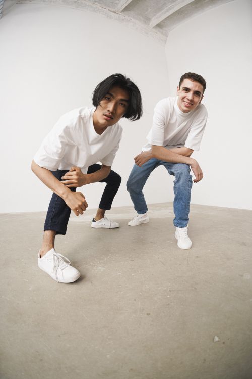 Free Two men in casual white shirts and jeans pose dynamically in a bright studio setting. Stock Photo