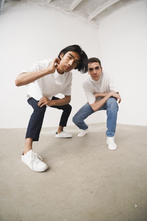 Free Two men crouching in a minimalist studio setting, showcasing casual fashion and modern style. Stock Photo