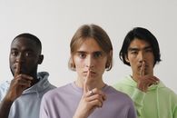 Three young adults making a shushing gesture in a studio setting, highlighting diversity.