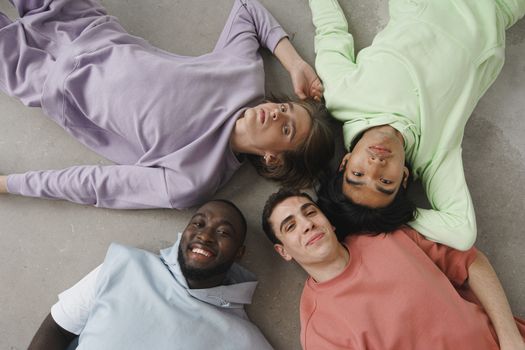 Top view of a diverse group of friends in pastel hoodies lying on the floor and smiling.