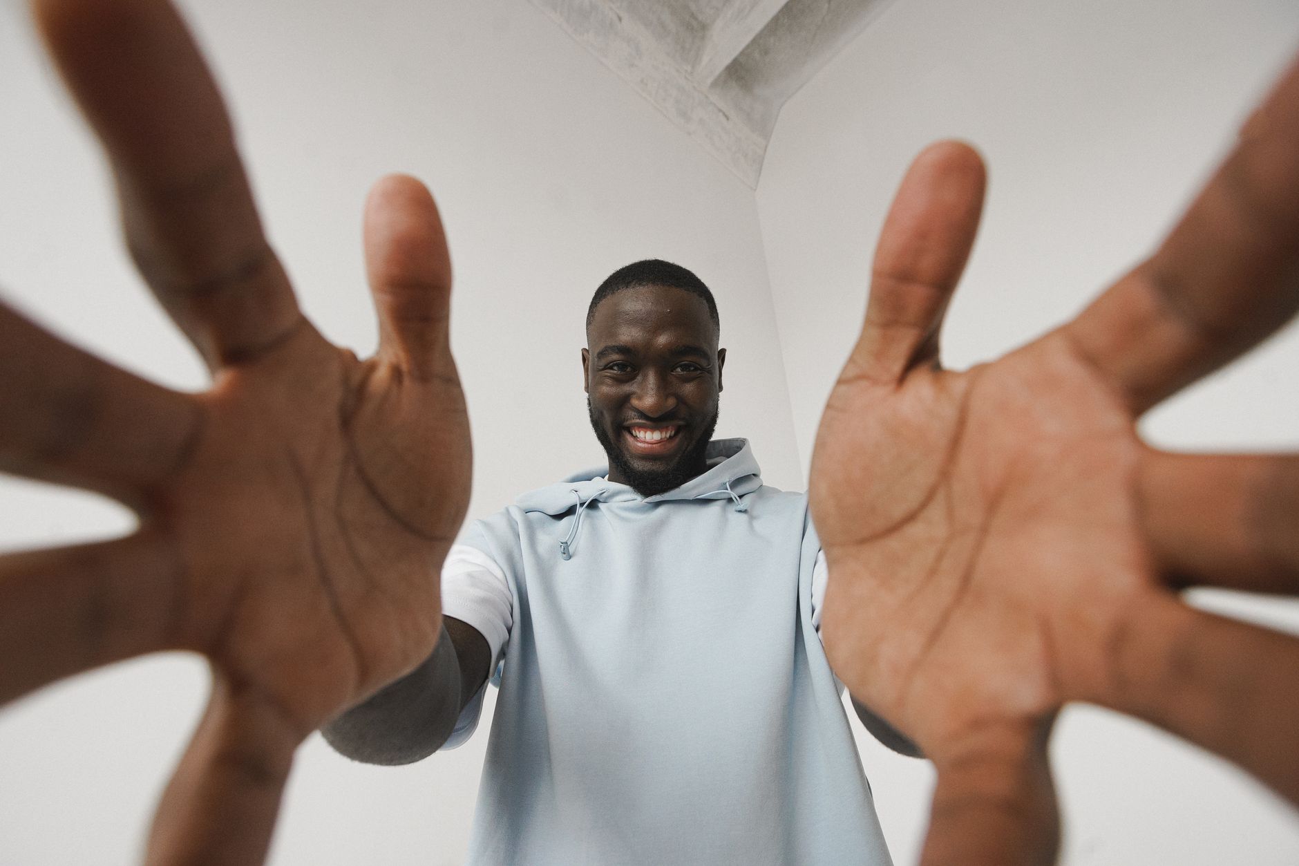Low-angle shot of a smiling African American man reaching towards the camera with both hands indoors.