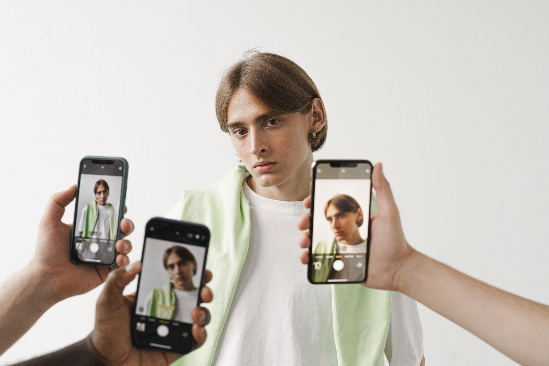 Jeune homme entouré de trois smartphones filmant son visage en gros plan sur fond blanc
