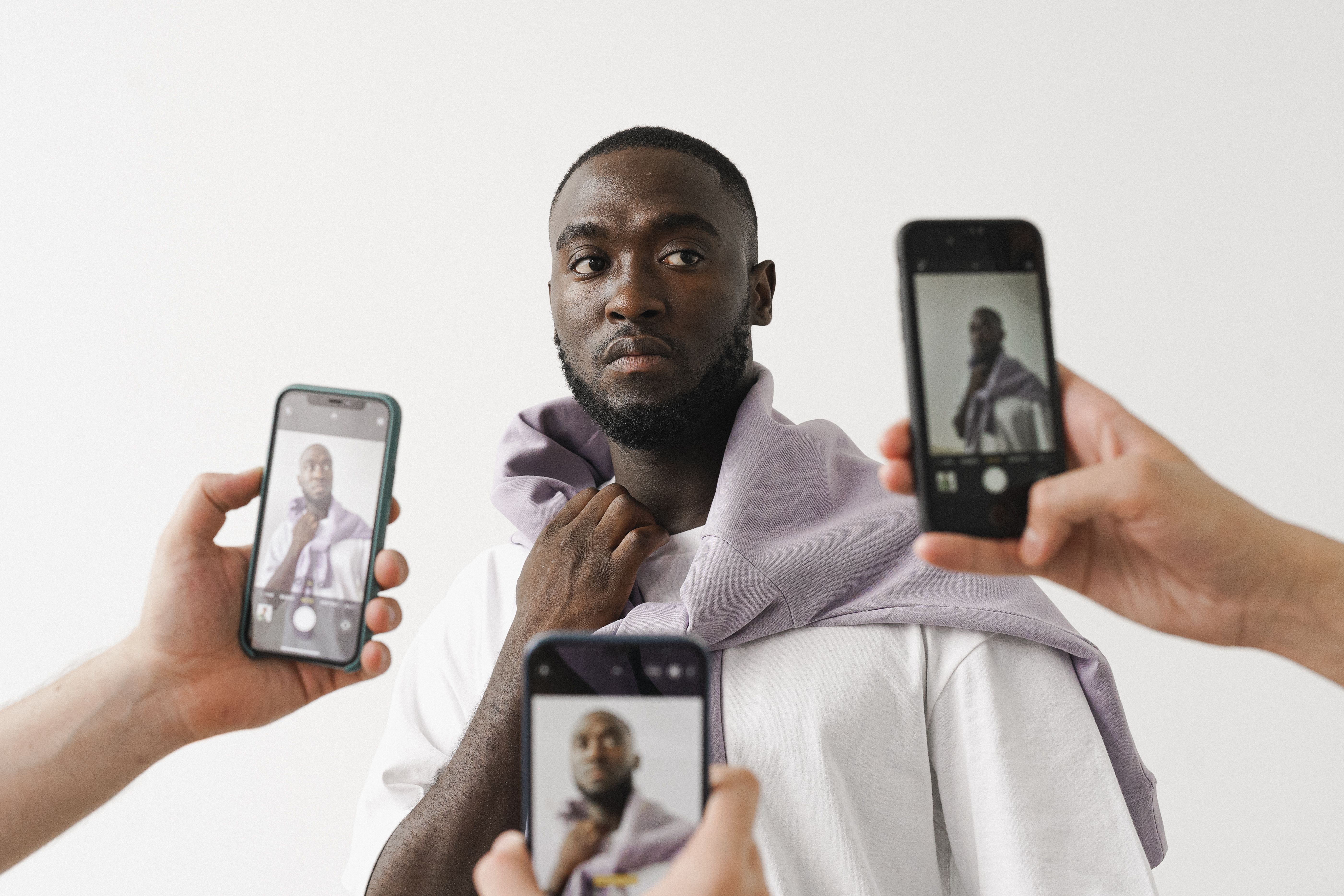 Three smartphones capturing a person wearing a cardigan around their neck