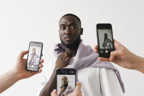Free Portrait of a stylish man surrounded by smartphones capturing his image indoors. Stock Photo
