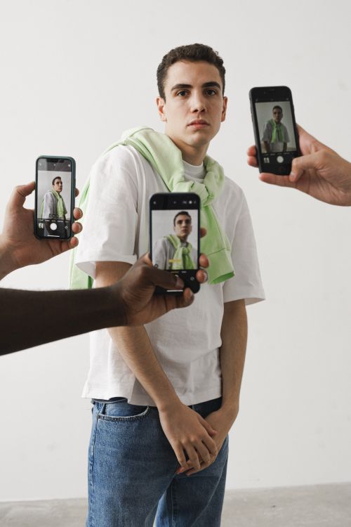 Free A casually dressed young adult poses while surrounded by smartphones capturing his image. Stock Photo