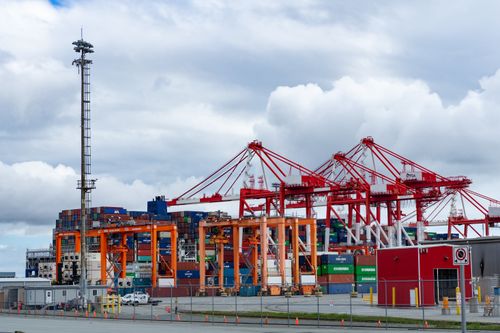 Free Vibrant cargo port with cranes and stacked containers against a cloudy sky. Stock Photo