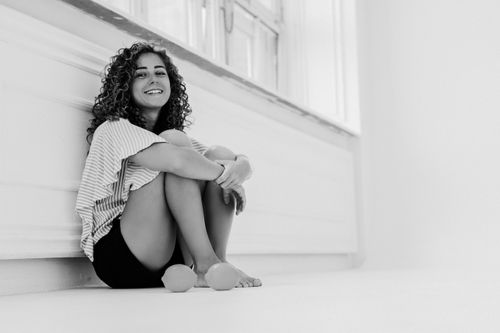 Free Black and white photo of a woman sitting against a wall, smiling warmly. Stock Photo