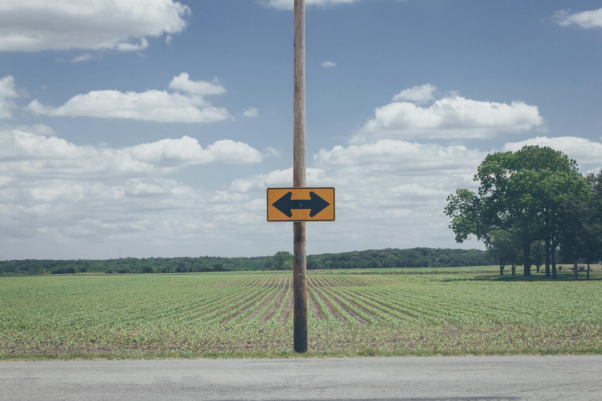 Scenic rural road sign on farmland with clear blue sky and clouds.