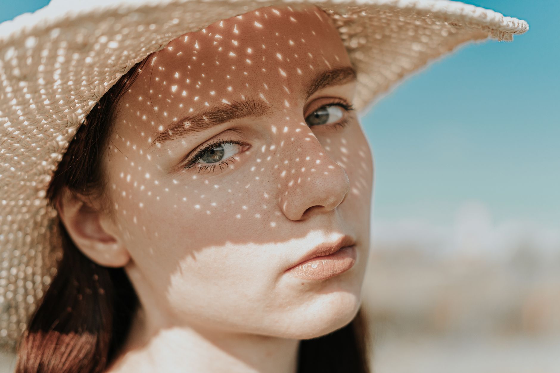 Young woman in straw hat casting intricate shadows on her face under bright sun.