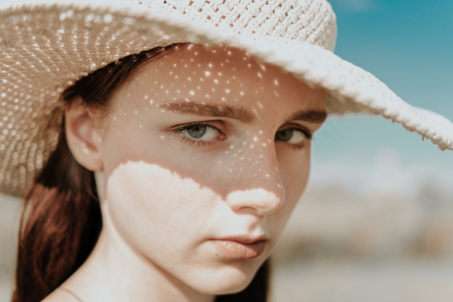 Close-up of a girl in a straw hat with sunlight casting patterned shadows on her face.