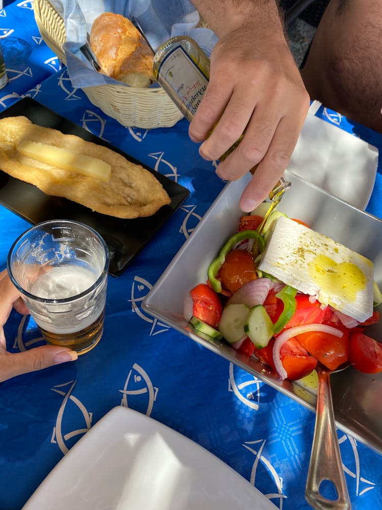 A Person Pouring Olive Oil On Salad