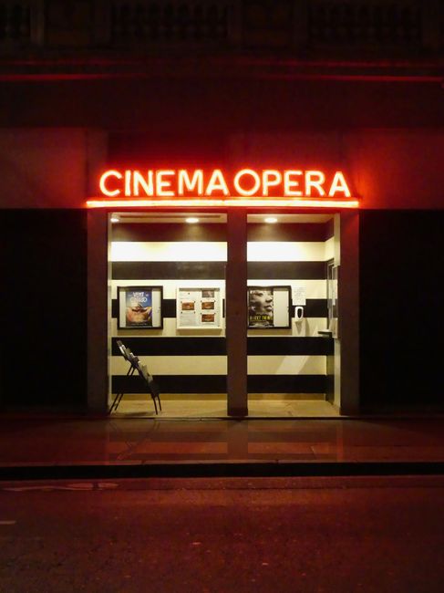 Night scene of the Cinema Opera entrance illuminated with neon lights, creating a vibrant urban atmosphere.