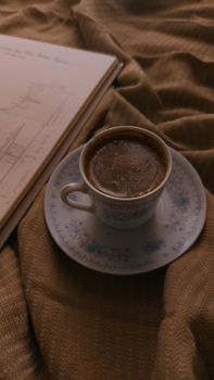 A warm cup of coffee placed on a textured blanket beside an open book, perfect for a cozy day.