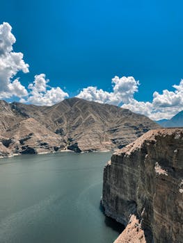 Majestic view of a serene lake surrounded by towering geological formations under a bright blue sky.
