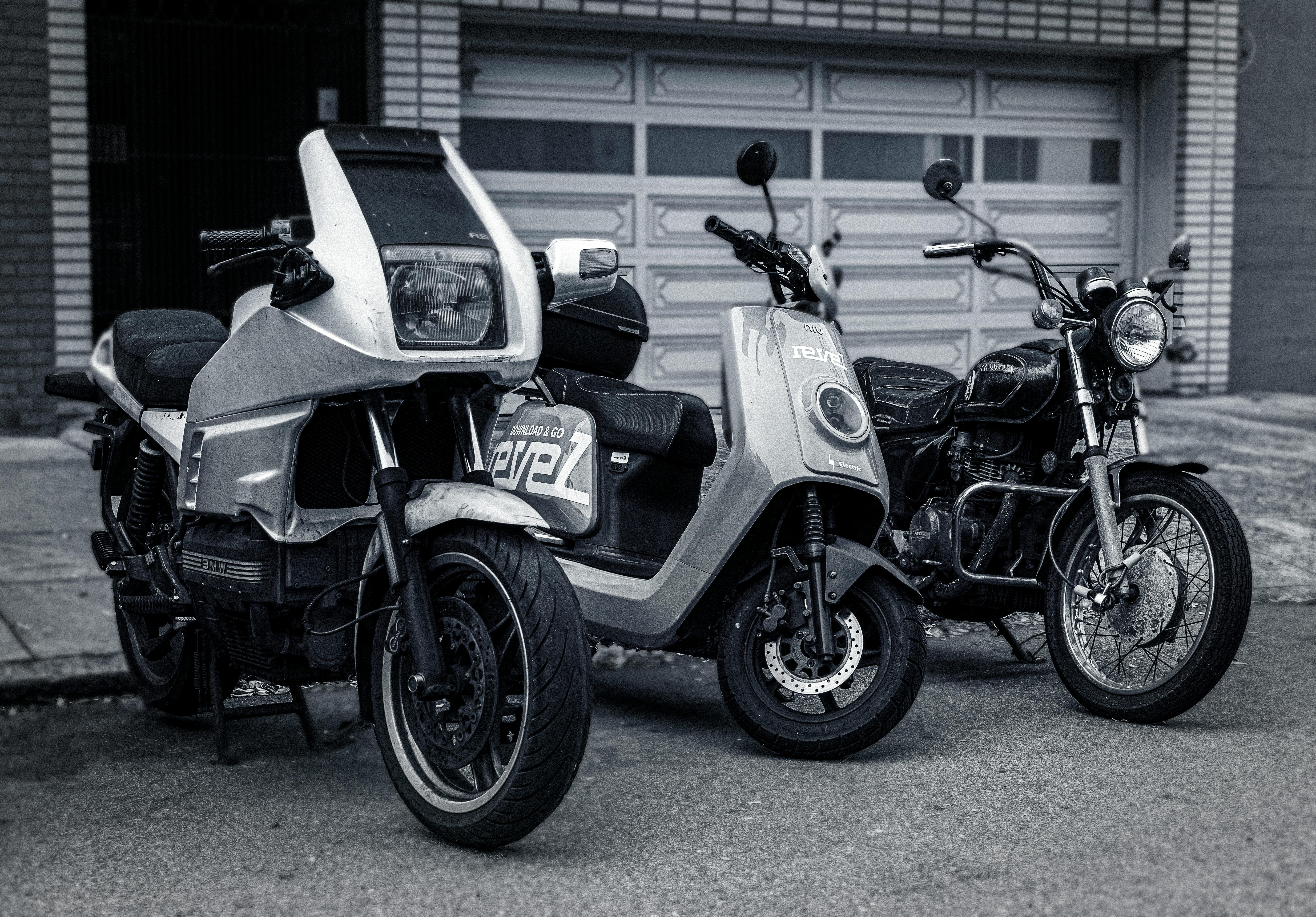 Free Black and white photo of vintage motorbikes parked on pavement in front of garage. Stock Photo