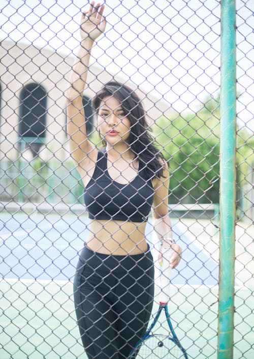 A Woman in Black Sports Bra and Leggings Standing Behind the Chain Link Fence