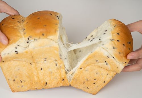 Free Close-up of hands tearing a delicious sesame loaf, highlighting its fluffy texture. Stock Photo