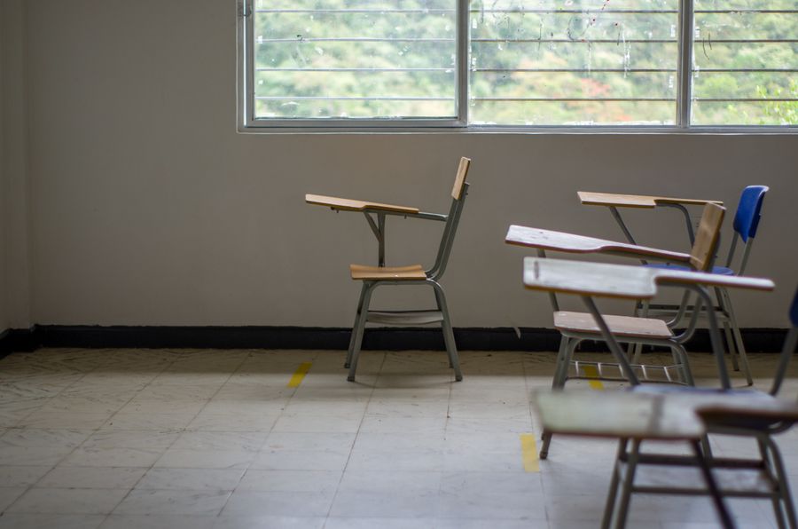 Quiet empty classroom interior with wooden school desks beside a large window