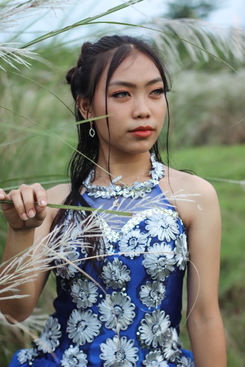 Free Elegant woman in a floral dress posing amidst green grass outdoors. Stock Photo