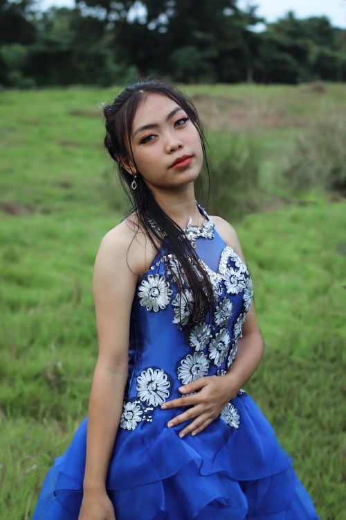 Free Young woman in a blue dress poses gracefully in a lush green outdoor setting. Stock Photo