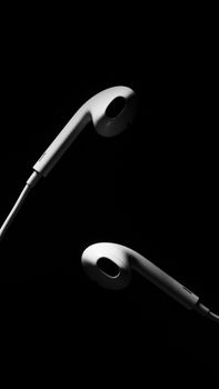 Monochrome close-up of two earphones against a black backdrop, emphasizing a minimalist design.