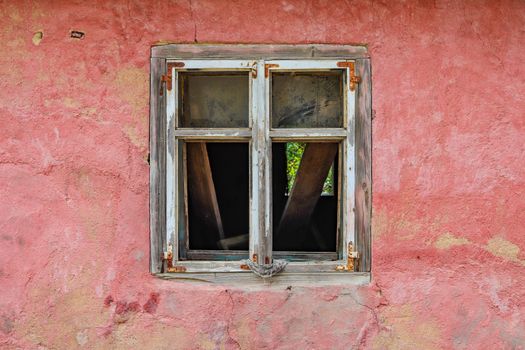 A vintage wooden window on a weathered red wall, showcasing rustic charm and decay.