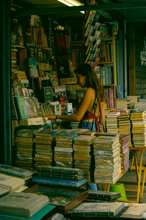 Free A woman exploring bookshelves filled with various books in an indoor bookstore setting. Stock Photo