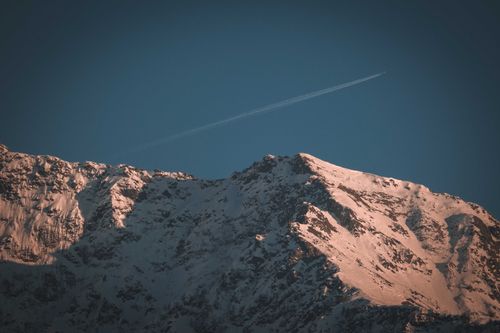 Free A serene view of a snow-covered mountain under a clear blue sky with a contrail. Stock Photo